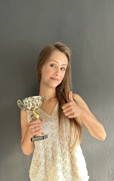Junge Frau hält einen Pokal und zeigt ein Daumen-hoch.